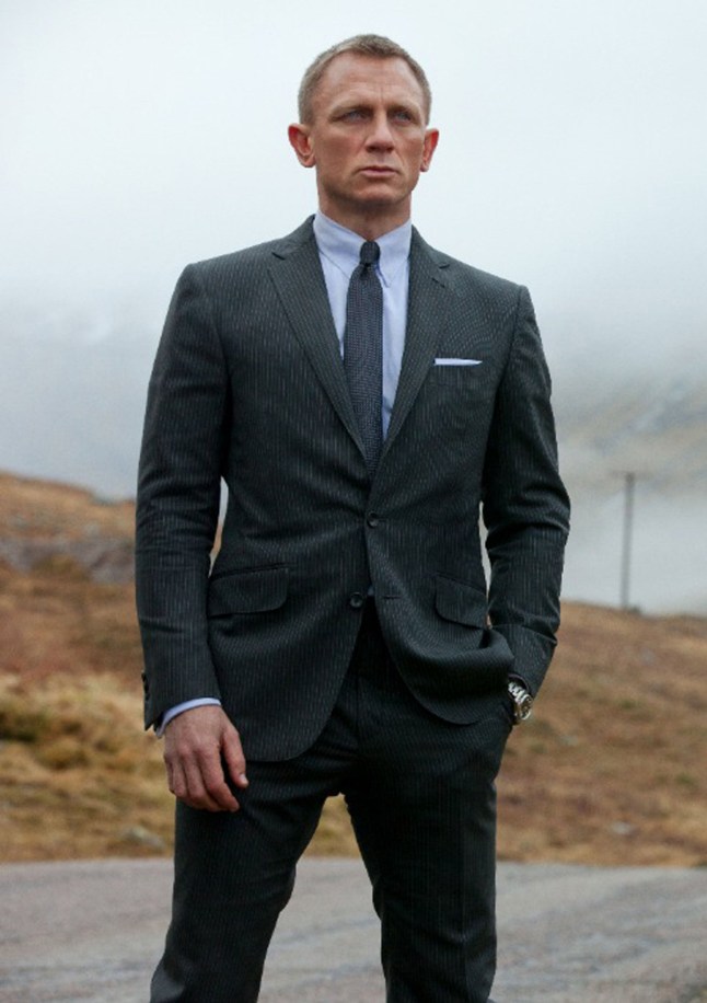 Daniel Craig stands in suit with hill behind him and foggy skies in scene from James Bond film Skyfall