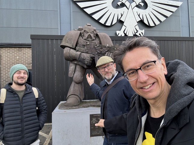 three men standing in front of Warhammer 40,000 statue
