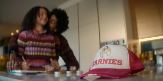 a man and woman kiss against kitchen counter with a white and red hat sitting by them