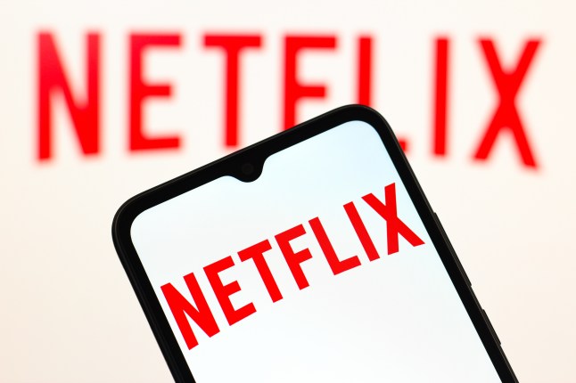 A red Netflix logo on a white background on a phone screen, with the same logo in the background on a screen behind.