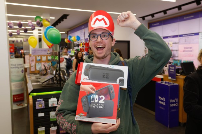 A man cheering as he holds his newly purchased Nintendo Switch 2 in a Currys store on launch day.