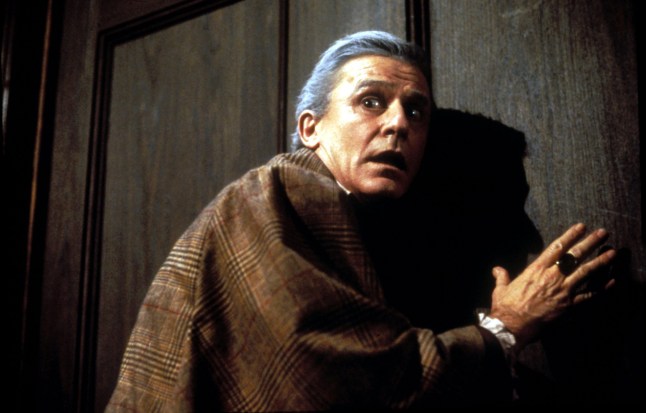Roddy Mcdowall as Peter Vincent cowers against a door with a tweed cloak in Fright Night