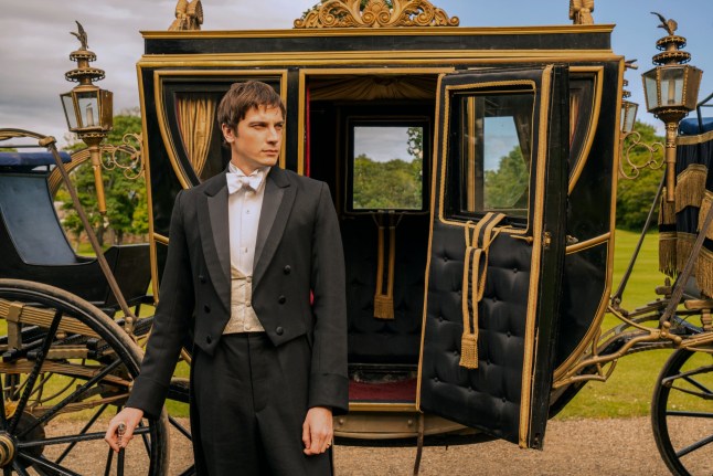 Guy Remmers as Theo in The Buccaneers standing in front of a carriage