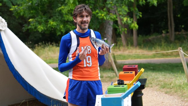 Matthew Baynton in a blue and orange sports team outfit holding a fish