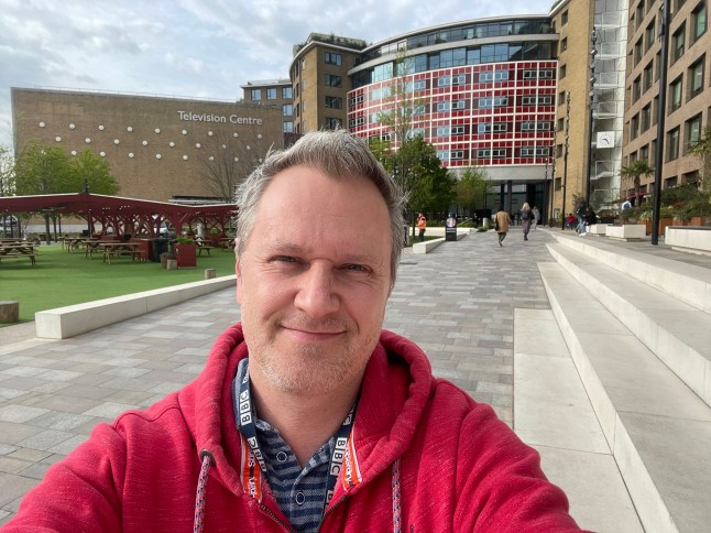 BBC presenter Duncan Newmarch wearing a red hoodie and taking a selfie outside a BBC building